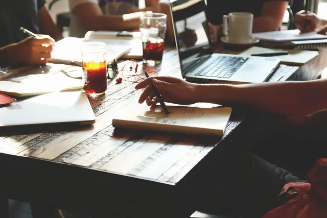 Reunião de trabalho com portátil, cadernos e apontamentos sobre a mesa