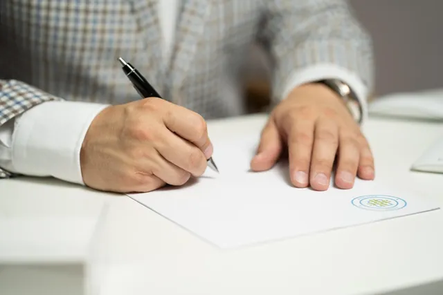 Mão a assinar um documento em cima de uma secretária