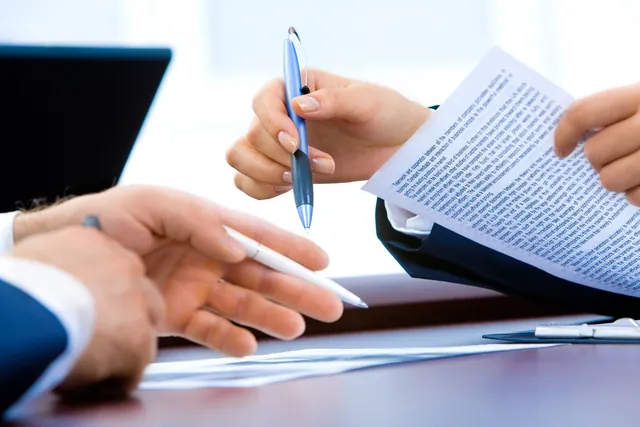 Duas pessoas a rever e a assinar um documento sobre a mesa